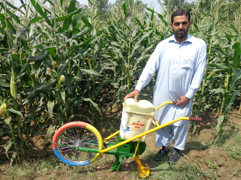 Maize farmer Raham Dil stands for a portrait with his push row planter. (Photo: Kashif Syed/CIMMYT)