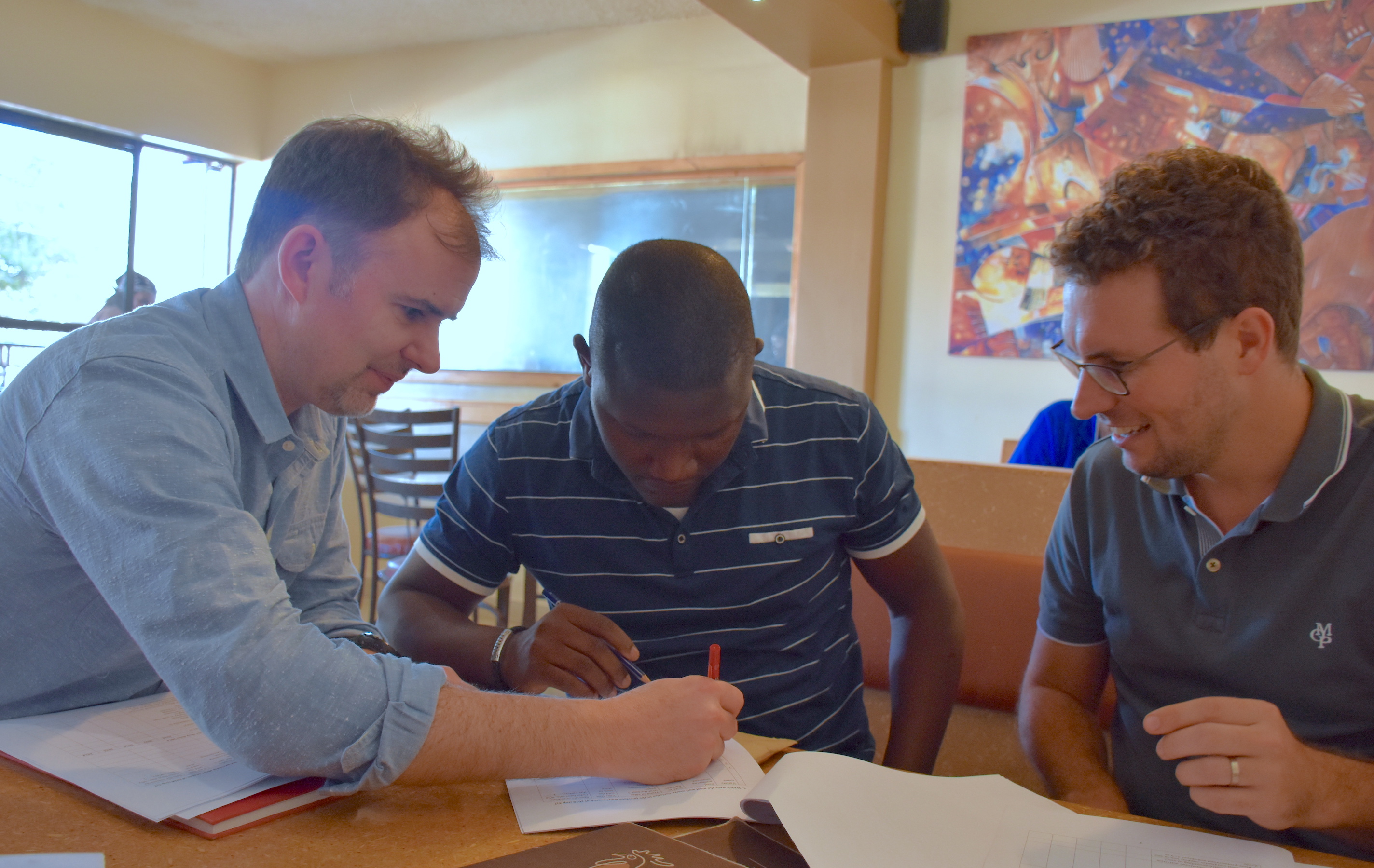 CIMMYT researchers Jason Donovan (left) and Pieter Rutsaert (right) discuss the research study questionnaire with consultant enumerator Victor Kitoto. (Photo: Jerome Bossuet/CIMMYT)