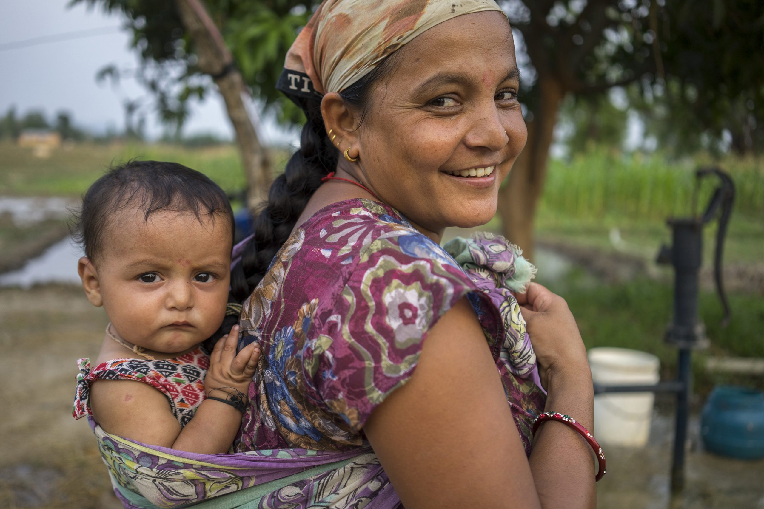Farmer Bhima Bhandari returns home after field work carrying her 7-month-old son Sudarsan on her back in Bardiya, Nepal. (Photo: Peter Lowe/CIMMYT)