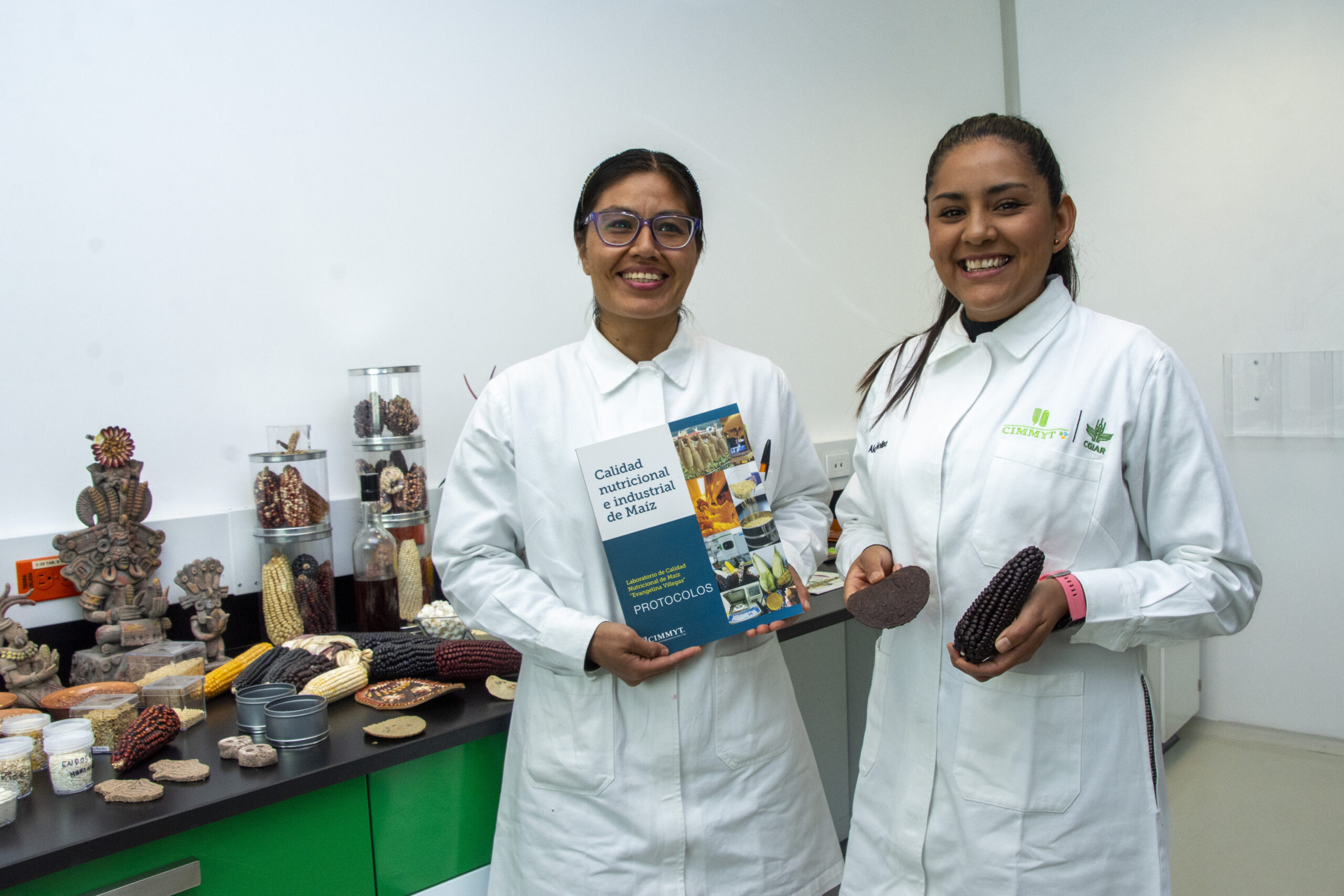 María Luisa Cabrera y Aidé Molina, asistentes de investigación asociadas en el Laboratorio de Calidad de Maíz de CIMMYT, muestran la diversidad de granos y productos derivados que se analizan para evaluar su calidad nutricional e industrial. (Foto: Jenifer Morales/CIMMYT)