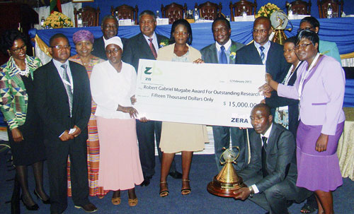 The Zimbabwe Maize Breeding Programme receives the Robert Gabriel Mugabe Award for Outstanding Research, at the10th Zimbabwe International Research Symposium, 13 February 2015. From left to right: Eng.G. Magombo (ZERA Chief Executive Officer); D. Kutywayo; Honorable O. Muchinguri-Kashiri (Zimbabwe Minister of Higher & Tertiary Education, Science &Technology Development); Dr. M.J. Tumbare; T. Chigama; P. Mphoko (Vice-President of the Republic of Zimbabwe); P. Mabodza; Honorable E.D Mnangagwa (Vice-President of the Republic of Zimbabwe); Dr. C. Mutimaamba; V. Tamirepi (holding trophy); P. Mazibuko; and Prof. I. Sithole-Niang; R. Mukaro. Photo: Courtesy of IBP